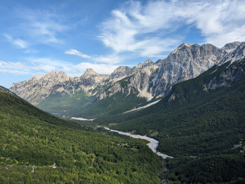 Grünes Tal durch das ein Fluß fliest mit schroffen Bergen im Hintergrund