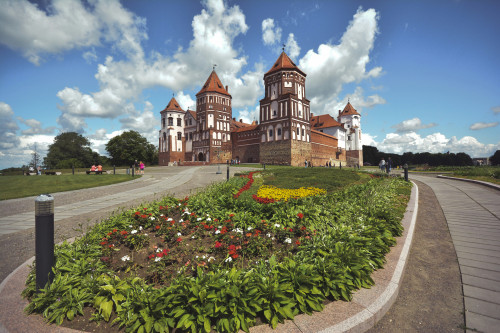Schlossanlage mit mehreren Türmen unter blauem Himmel mit Beet im Vordergrund